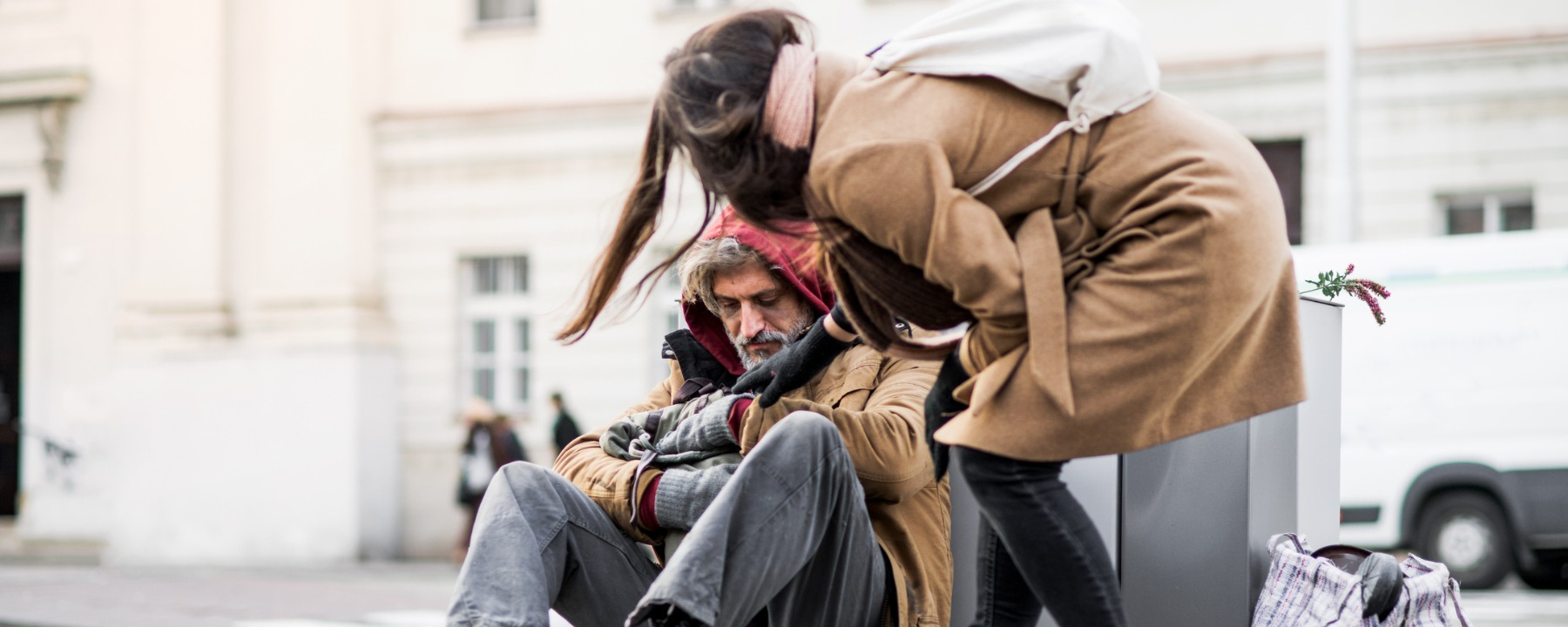 Young woman giving money to homeless beggar man sitting in city