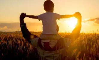 Customer experience - Father carrying son on shoulders in field of wheat at sunset
