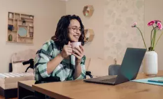Young businesswoman in a wheelchair enjoying coffee and working online from home 