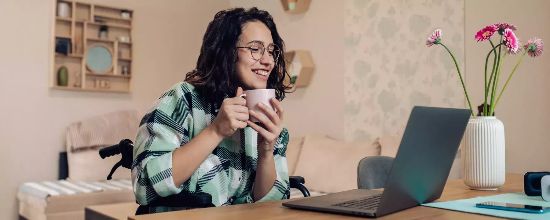 Young businesswoman in a wheelchair enjoying coffee and working online from home